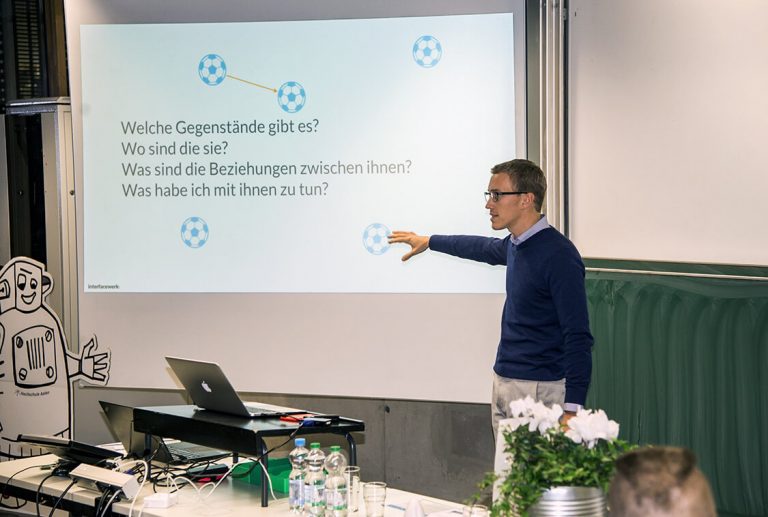 Moritz Tuerck steht vor einer Leindwand in einem Hörsaal und spricht zu den Zuhörern